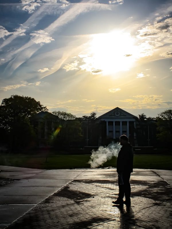 A silhouetted figure on an empty University of Maryland walkway, early morning sun behind the trees.