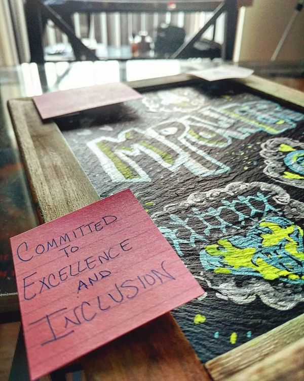 Chalkboard: MPOWER in patterned letters, with sticky notes reading Committed to Excellence and Inclusion.
