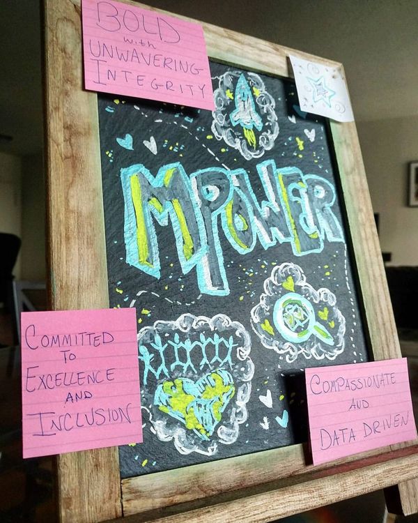 Chalkboard: MPOWER with a rocket and a heart, framed by sticky notes: Bold and Unwavering Integrity, Committed to Excellence and Inclusion, Compassionate and Data Driven.