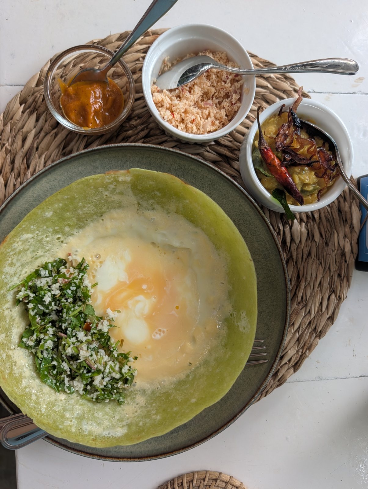 An egg hopper with green batter, coconut sambol, chutney and a dhal with a red chili, shot from above.