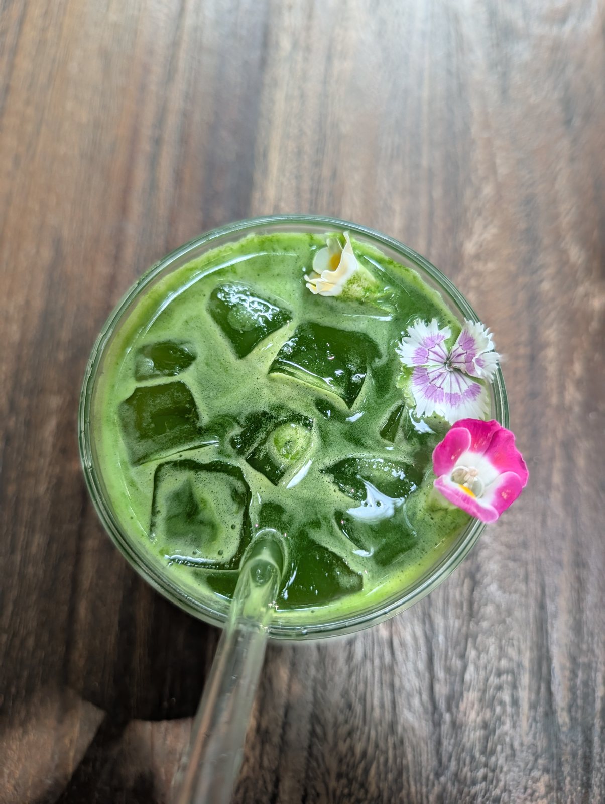 A green iced drink topped with small pink and white flowers.