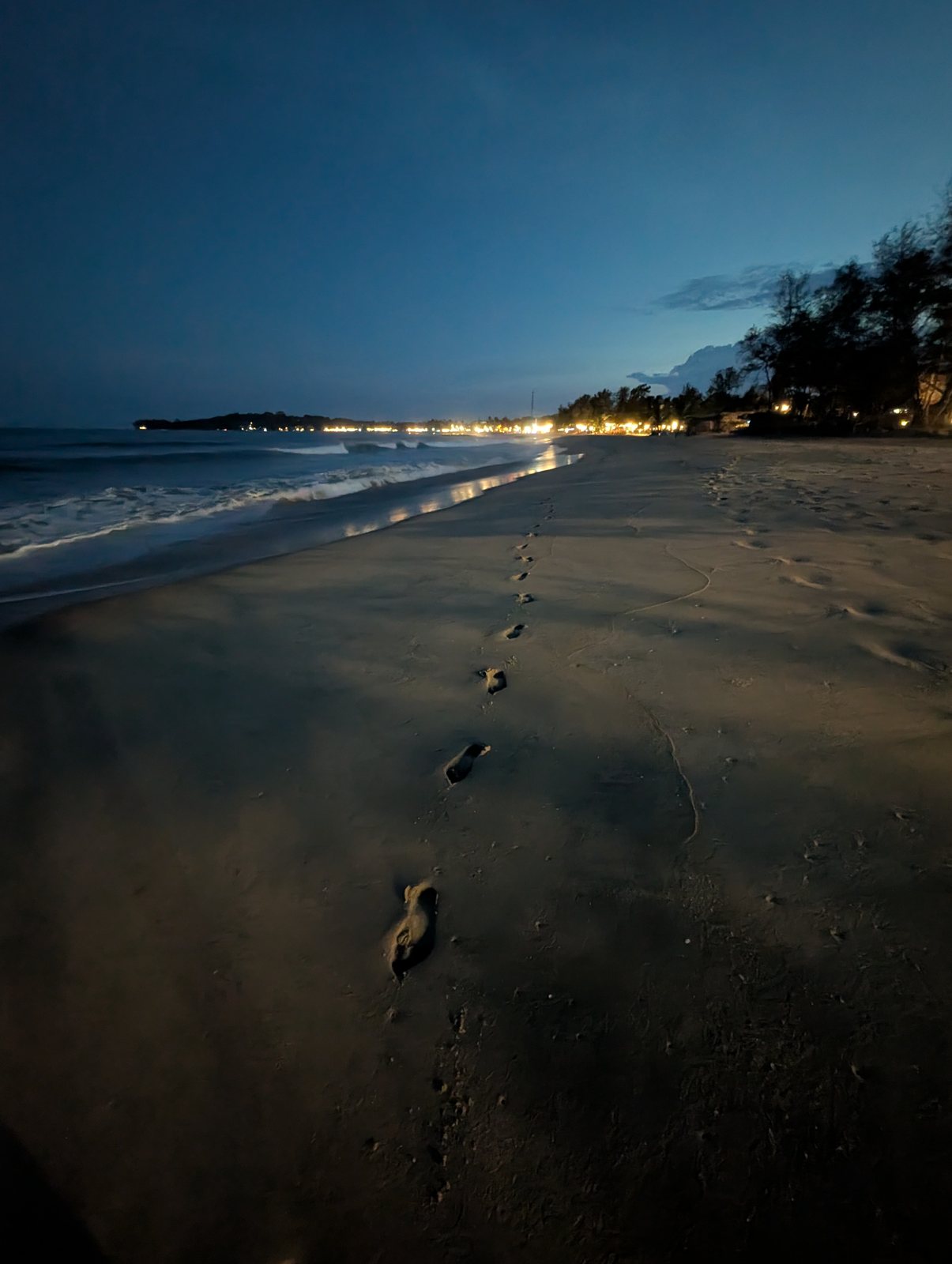 Footprints on a Sri Lankan beach at night, with lights along the shore.